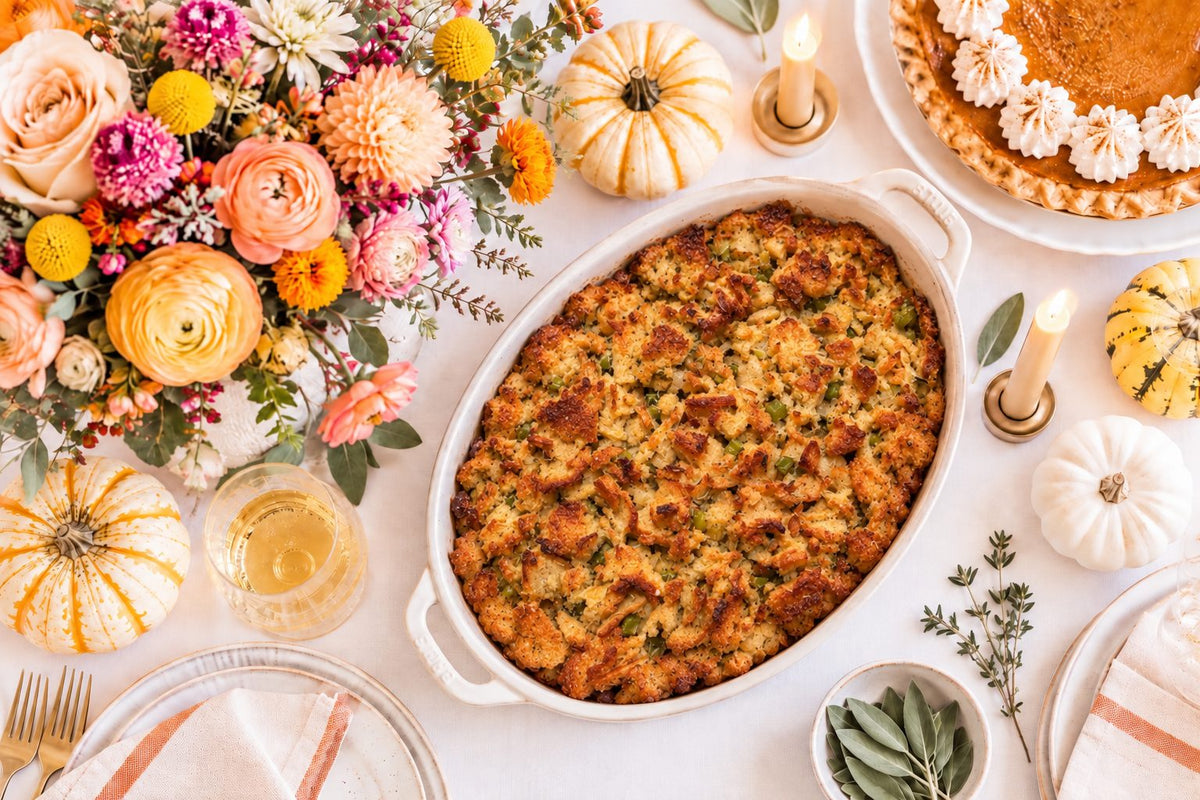 Everything bagel stuffing baked golden and crisp in a white oval dish, on a Thanksgiving table with autumn flowers, small pumpkins and pumpkin pie